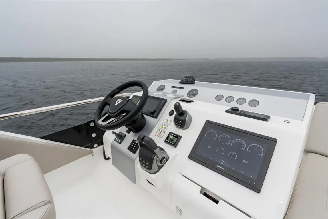 Boat dashboard featuring steering wheel, digital displays, and gauges, with a misty water view in the background.